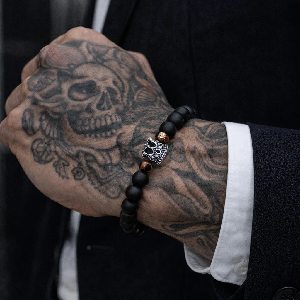 Person wearing a black beaded bracelet with a skull charm on a tattooed arm.
