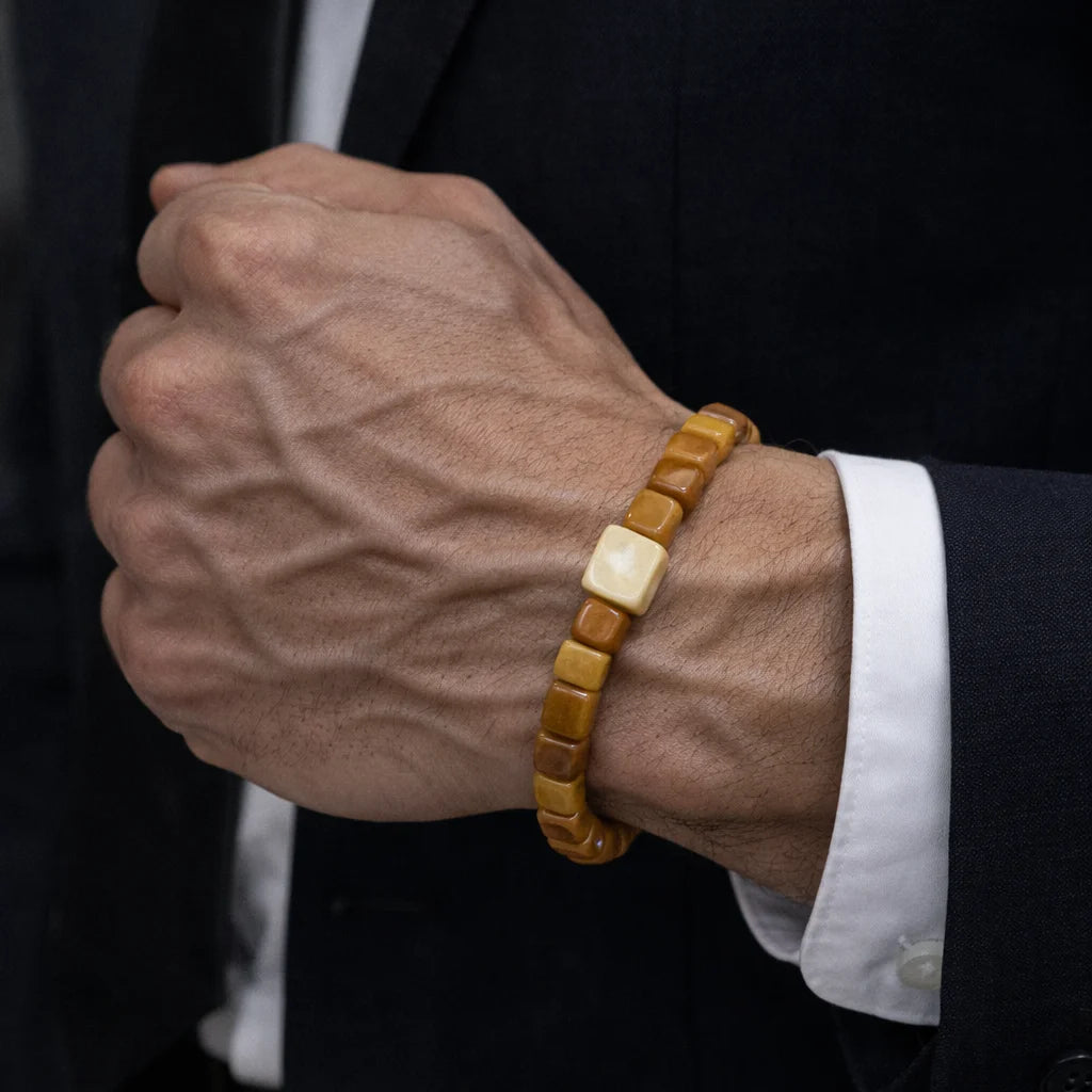 Hand wearing a wooden bracelet with a dark suit and white shirt background