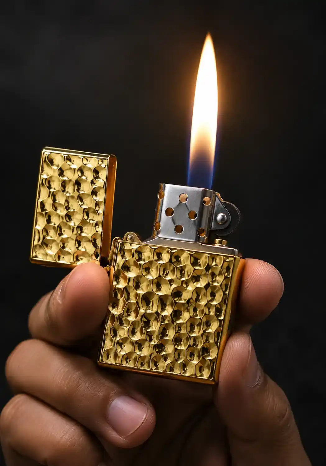 A close-up of a hand holding a gold textured lighter with a bright flame lit against a dark background.
