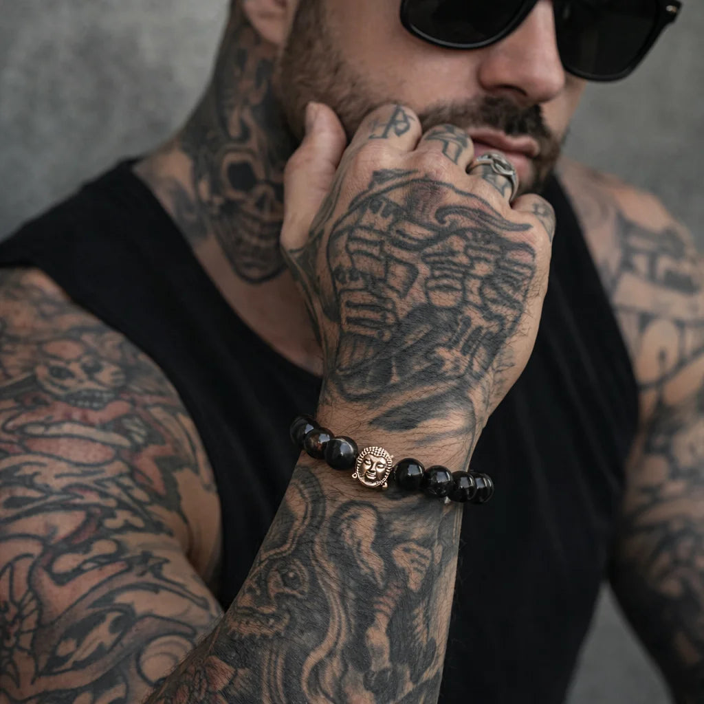 Man with tattoos on arms and face wearing sunglasses, black shirt, and black beaded bracelet.