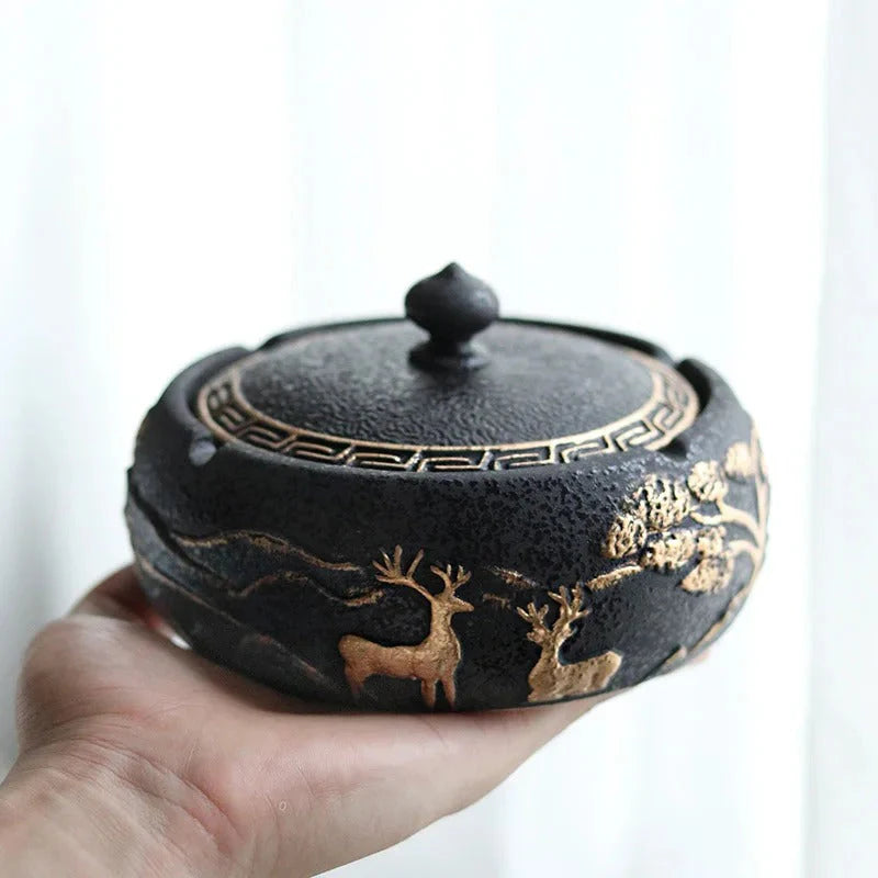 Decorative black Ashtray with gold deer design held in a hand against a white background