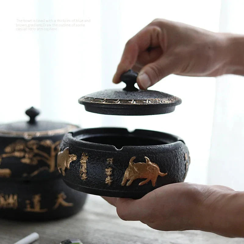 Person opening a black ceramic ashtray with gold designs on a light background