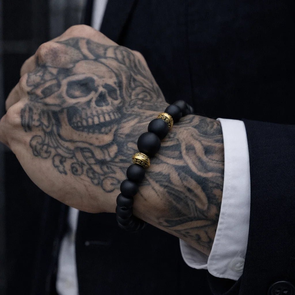 Person wearing a black beaded bracelet with a gold accent on a tattooed wrist.