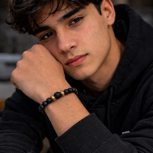 Person wearing a black beaded bracelet with gold accents, sitting indoors.