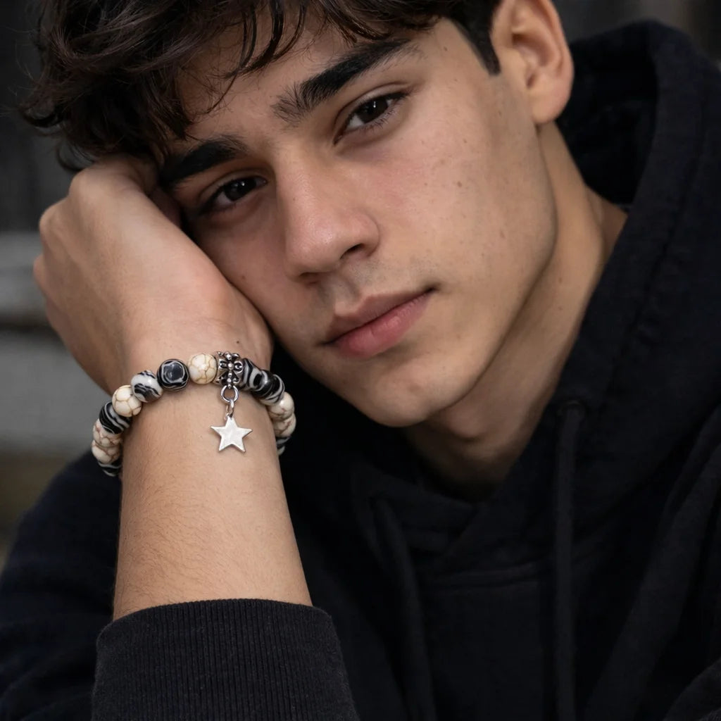 Person wearing a bracelet with star charm, sitting against a dark background