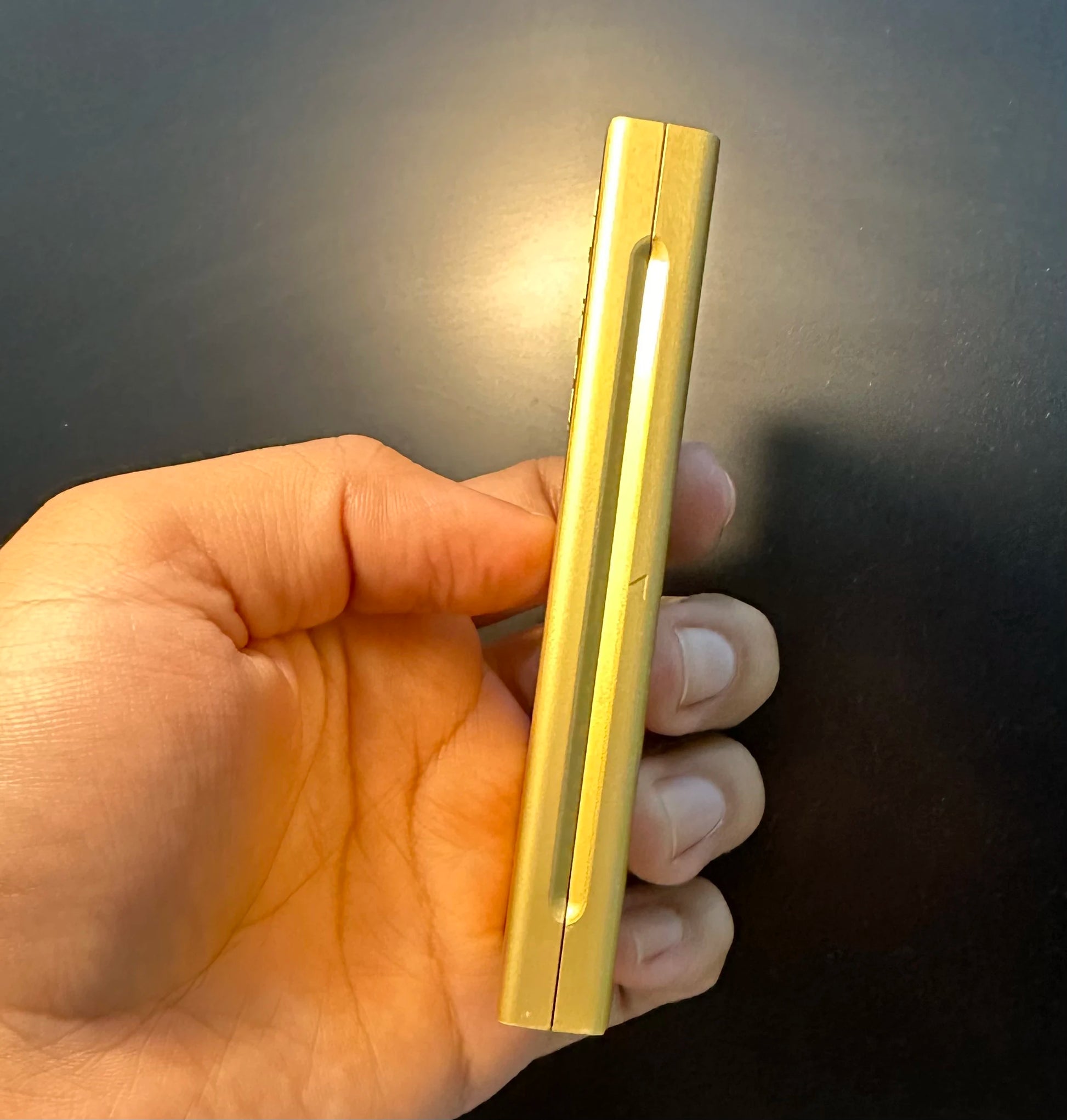 Gold lighter held in a hand against a dark background