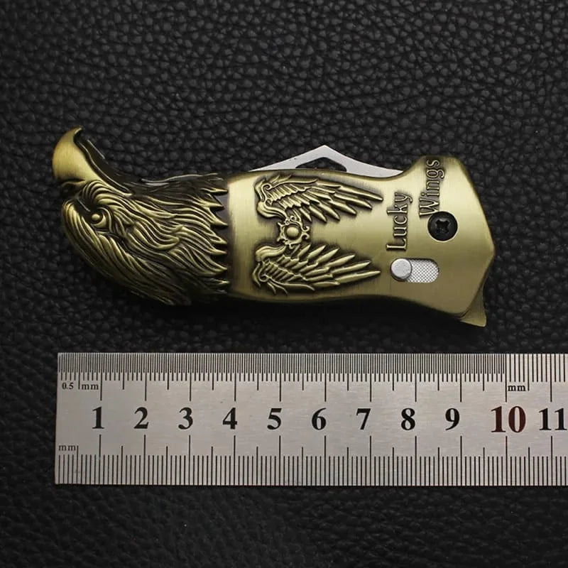 Gold-colored knife with eagle design on a black textured background, accompanied by a ruler for scale.
