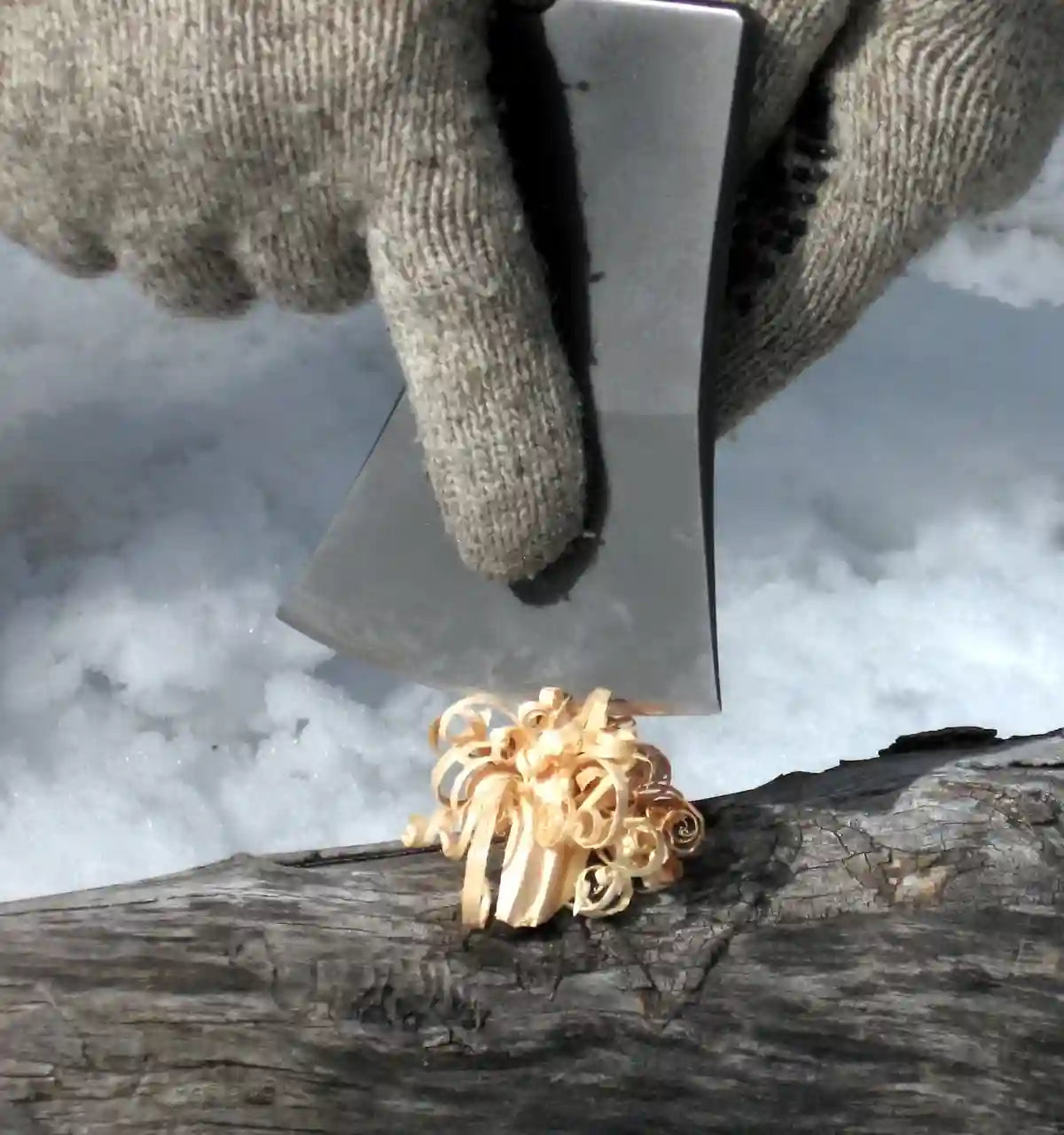 Gold ring on a log with a hand holding a metal tool above it, on a snowy background