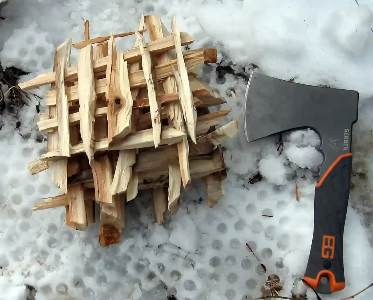 Wooden kindling pile on snow with an axe