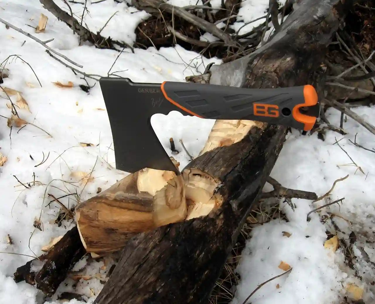 Axes with black and orange handles on a log in a snowy forest setting