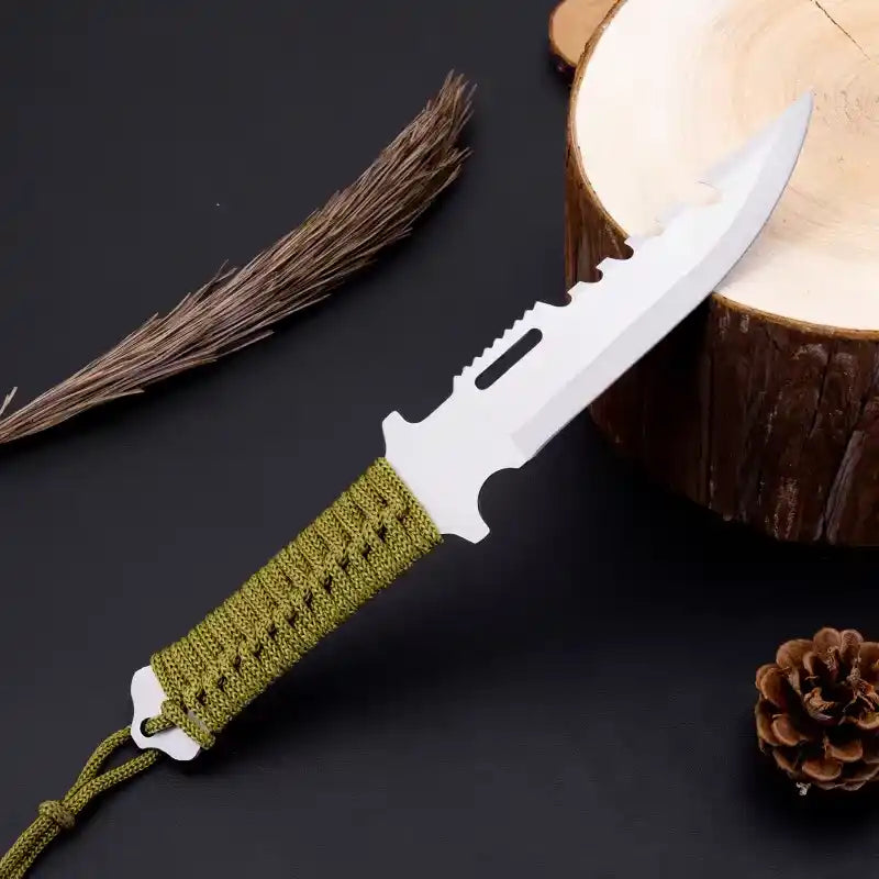 Knife with a green handle on a dark surface with a wooden log and pine cone.