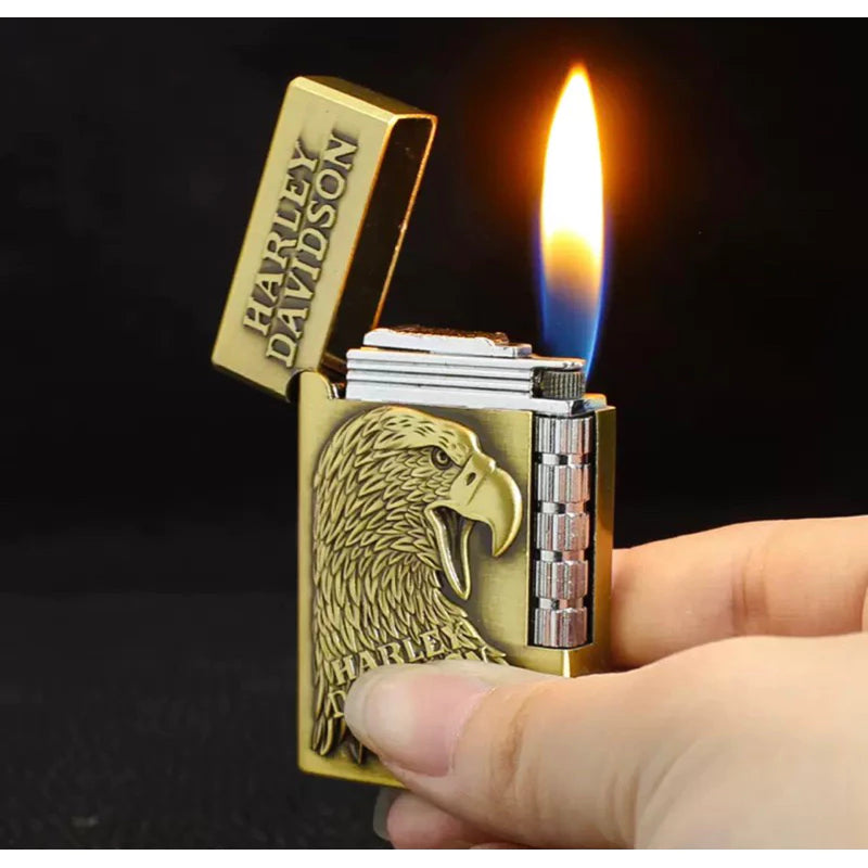 A hand holding a Harley-Davidson lighter with an open flame, featuring a gold-toned metal body with an embossed eagle design and the Harley-Davidson brand name on the lid.