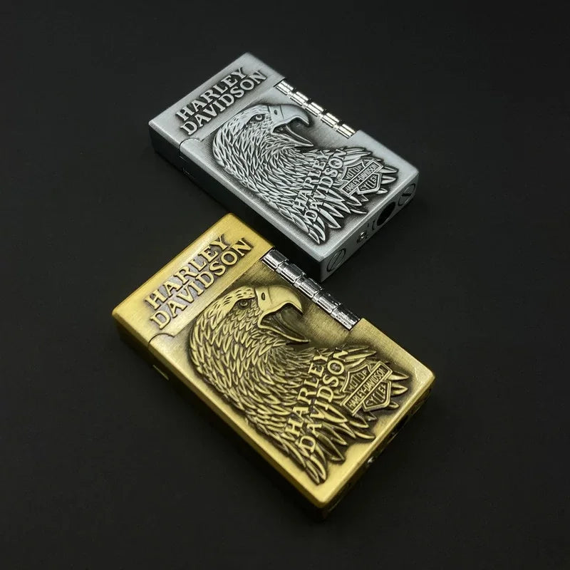 Two Harley-Davidson lighter-style cases shown on a black background, one in silver and one in gold, both with an embossed eagle and logo design.