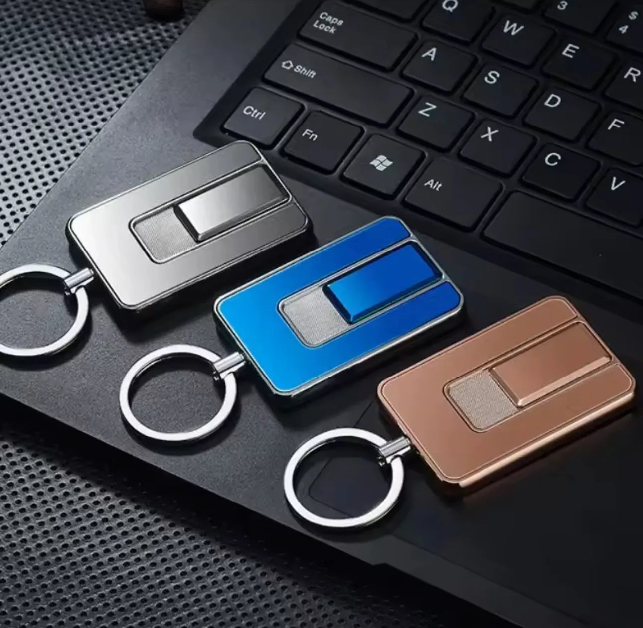 Three keychains lighter in silver, blue, and bronze on a black keyboard