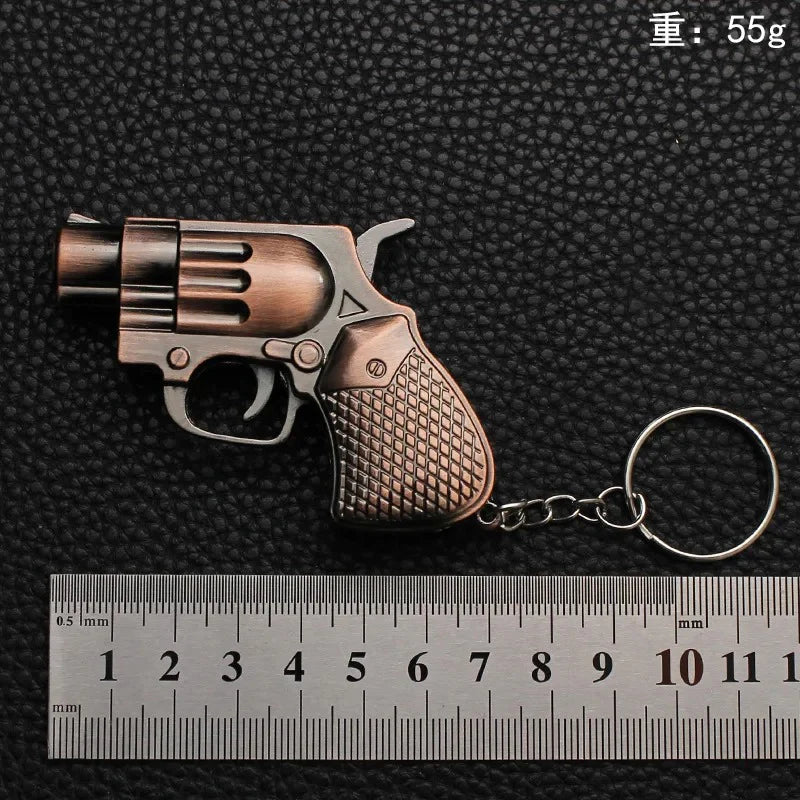 Bronze revolver-shaped Lighter with keychains on a black textured background with a ruler for scale.