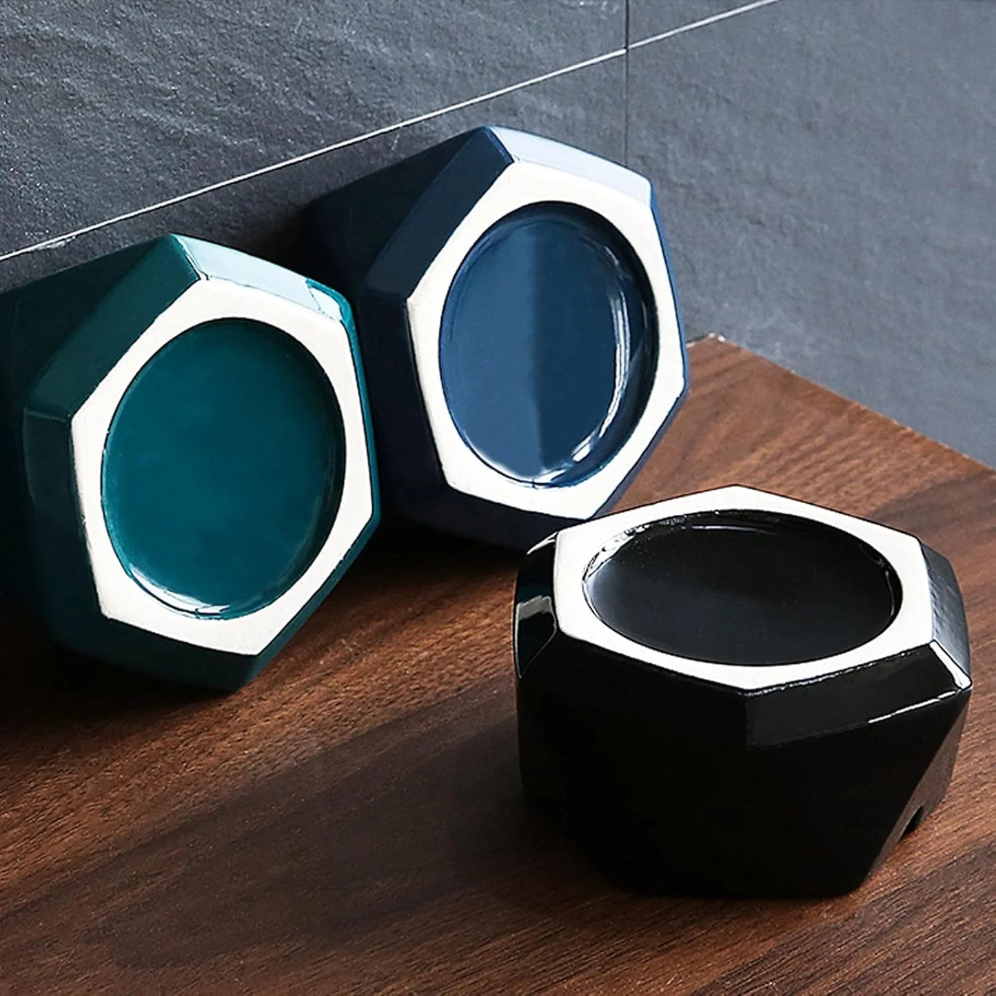Three hexagonal Ashtray, blue, and black on a wooden surface with a gray tiled wall background.