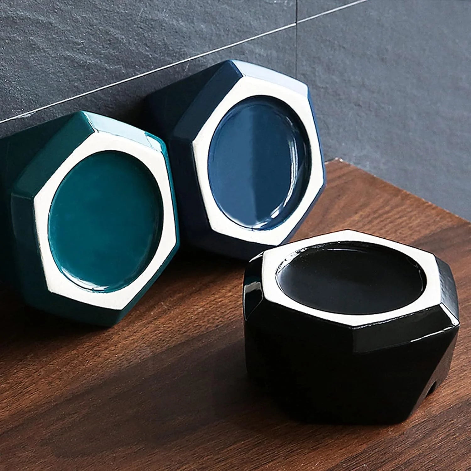 Three hexagonal Ashtray, blue, and black on a wooden surface with a gray tiled wall background.