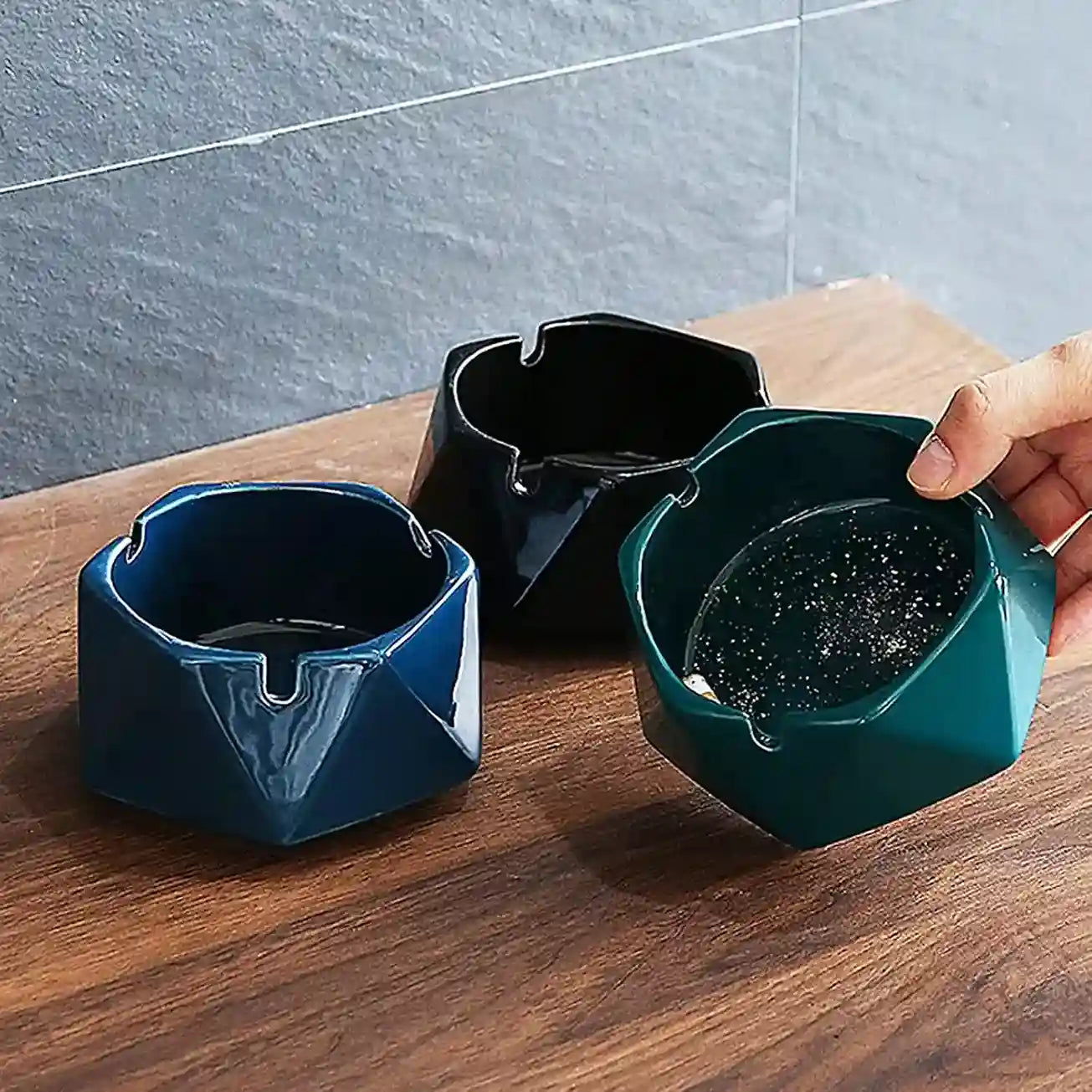 Three geometrically shaped ashtrays in different colors on a wooden surface.