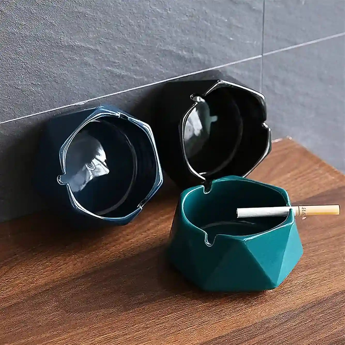 Teal geometric ashtray with a lit cigarette on a wooden surface.