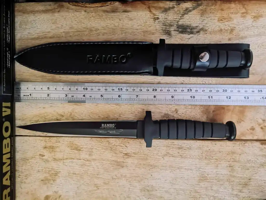 Two knives with sheaths labeled 'Rambo' on a wooden surface with a ruler for scale.