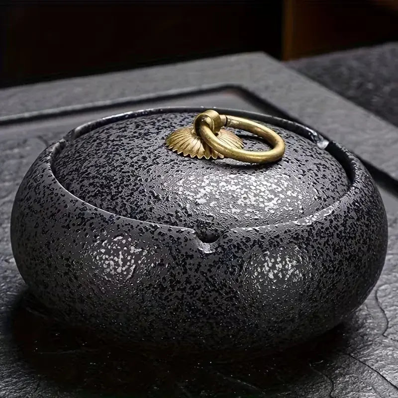 Black ceramic Ashtray with a gold lid on a dark surface