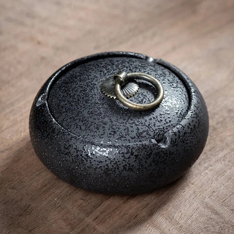 Black speckled ceramic Ashtray with a metallic ring on a wooden surface