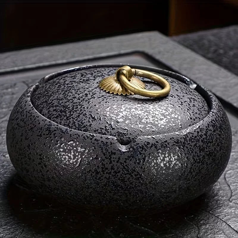 Black ceramic Ashtray with a gold lid on a dark surface