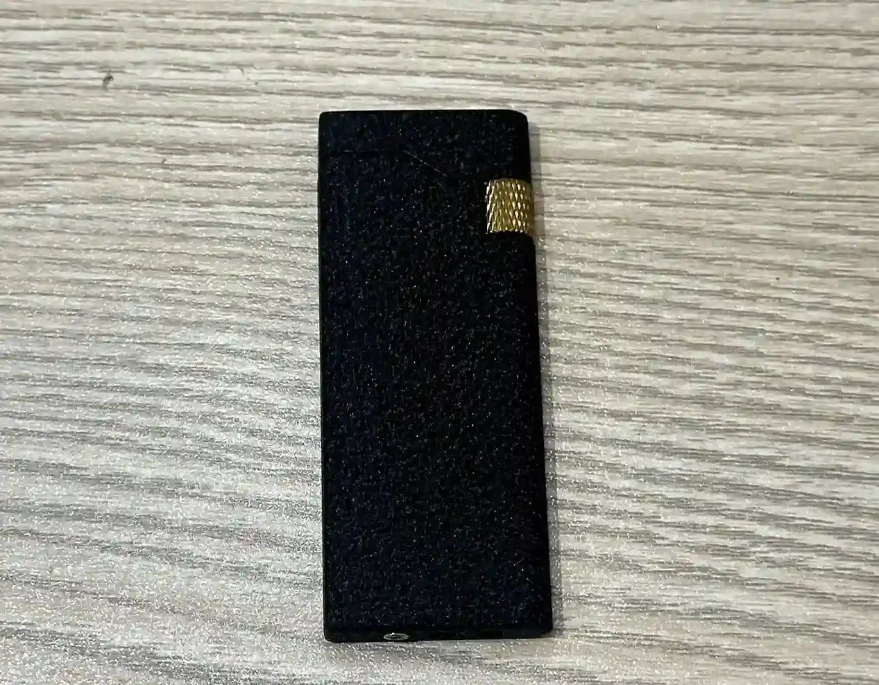 Black lighter with gold accent on a textured gray surface