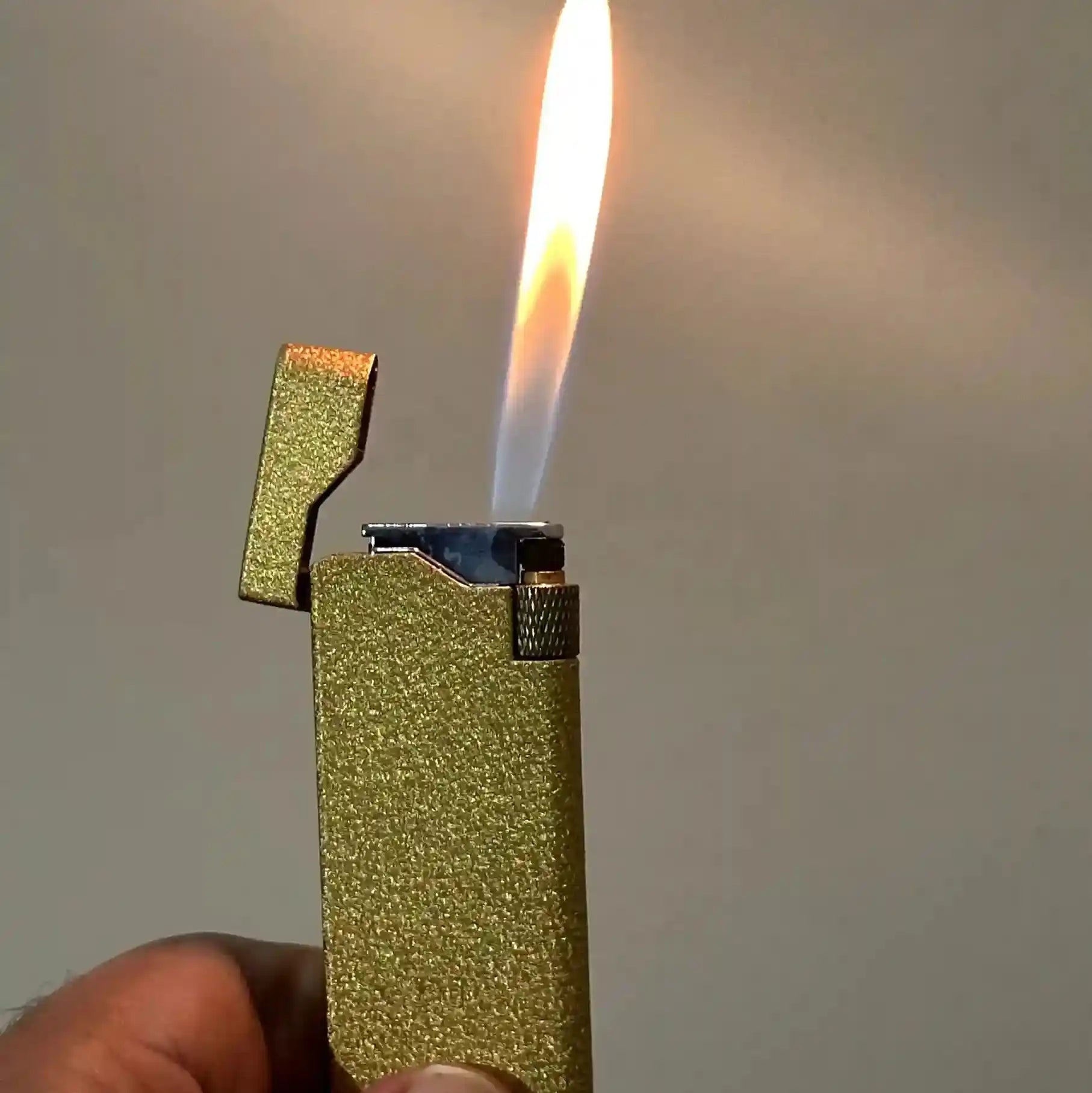 Gold lighter with a flame against a neutral background