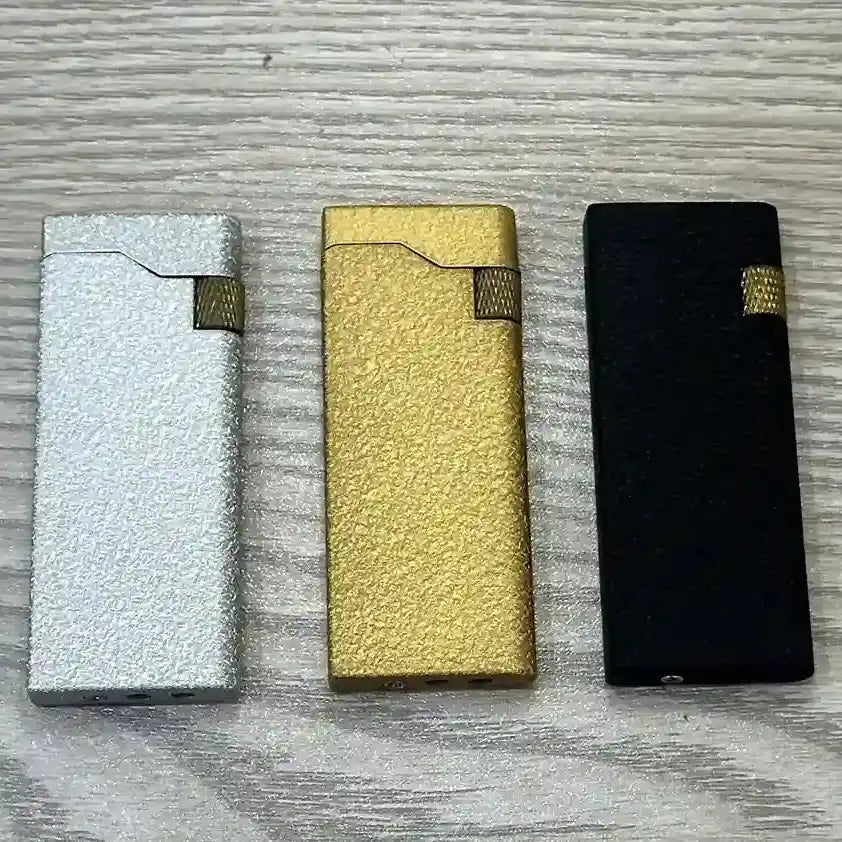 Three metallic lighters in silver, gold, and black on a textured surface
