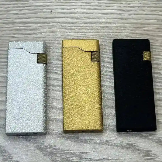 Three metallic lighters in silver, gold, and black on a textured surface