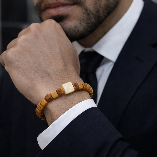 Man wearing a wooden beaded bracelet on his wrist, dressed in a suit.