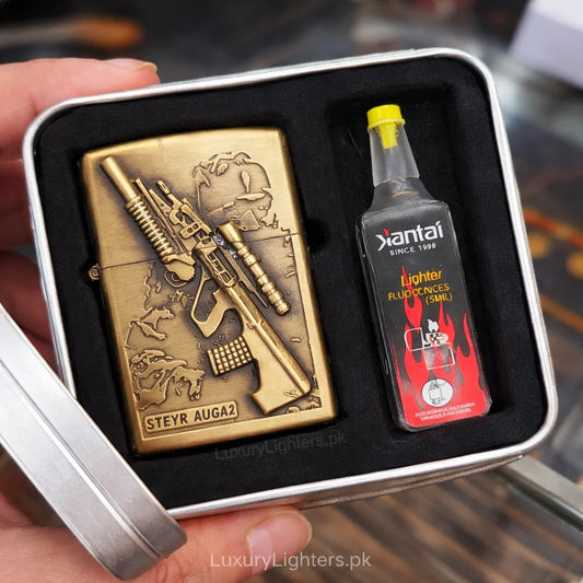 Brass lighter with rifle design and bottle of fuel in a box, held by a hand.