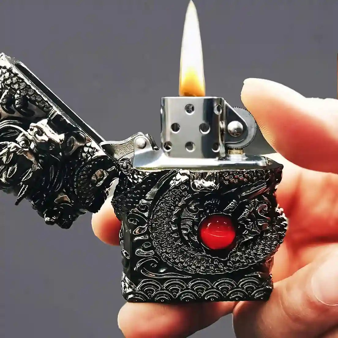 Decorative lighter with intricate designs and a red gem held by a hand against a dark background