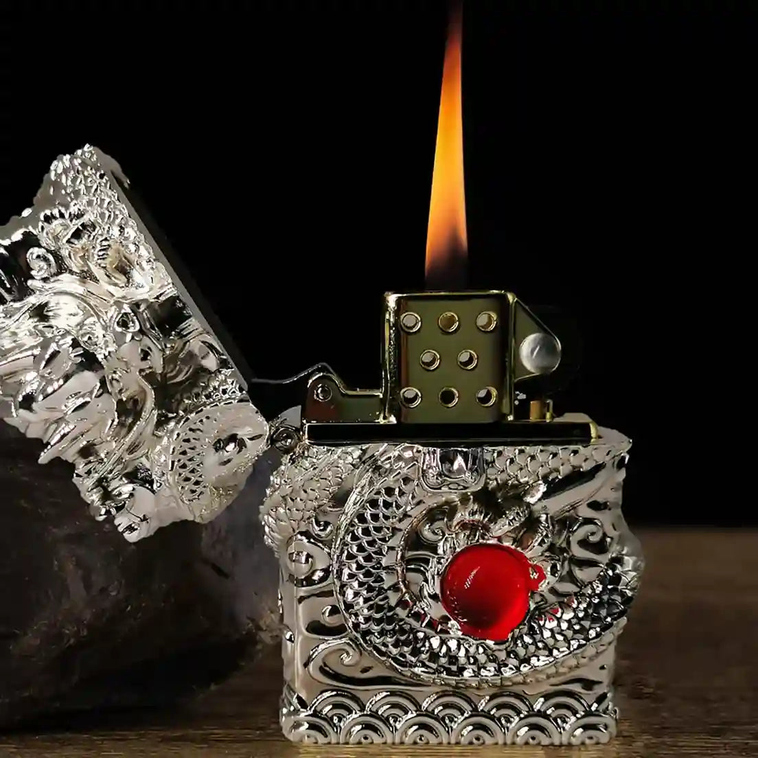 Decorative lighter with intricate designs and a red gemstone, lit on a dark background.